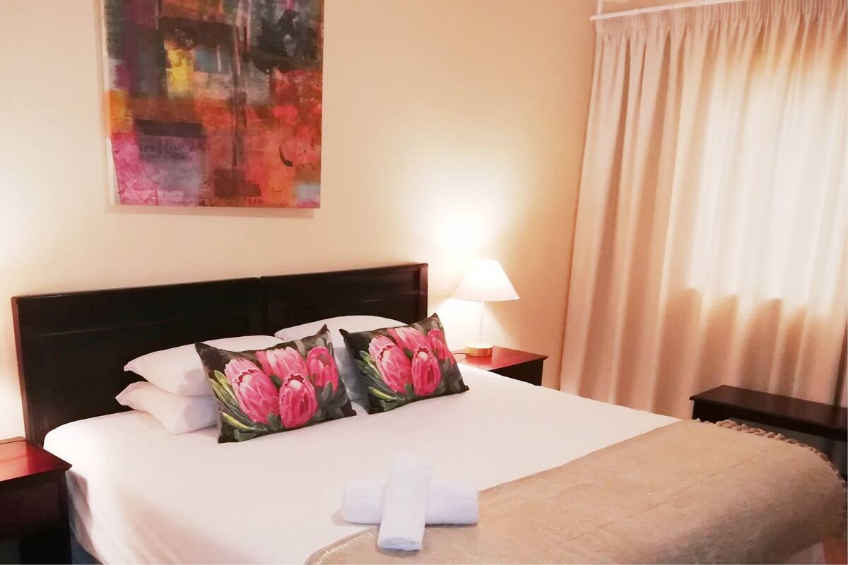 A neatly made bed with floral pillows, two bedside lamps, and a painting on the wall.