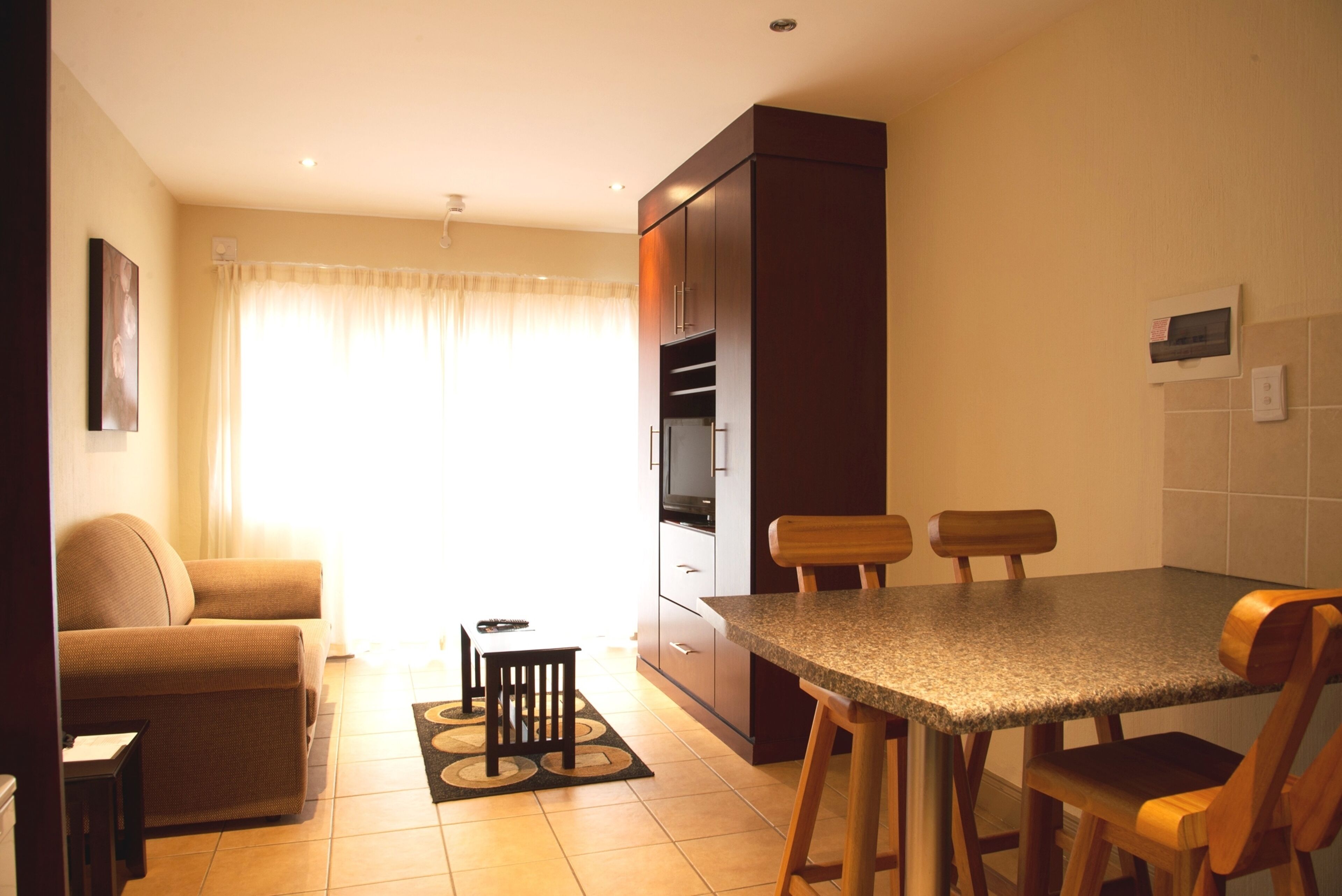 Un espacio habitable compacto con kitchenette, una zona de comedor con mesa y sillas, un sofá y una pequeña mesita auxiliar.