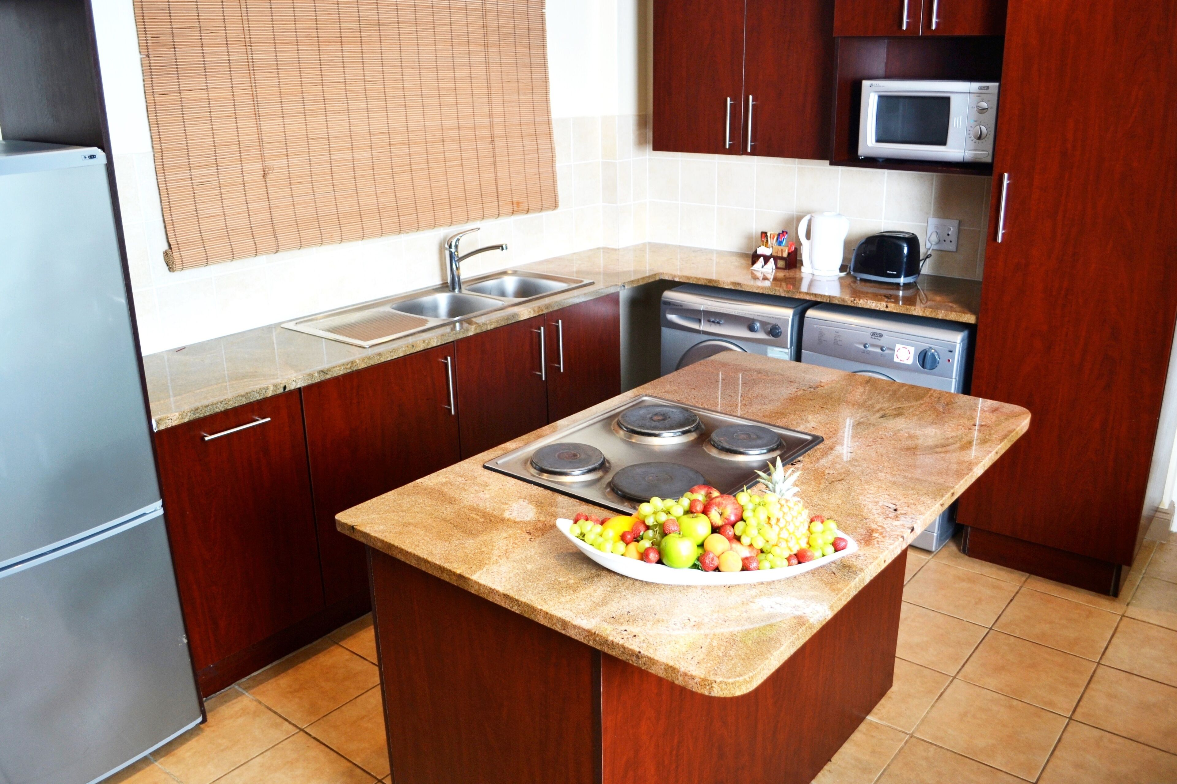 Una cocina con armarios de madera, encimera de granito, estufa integrada, microondas y lavavajillas.