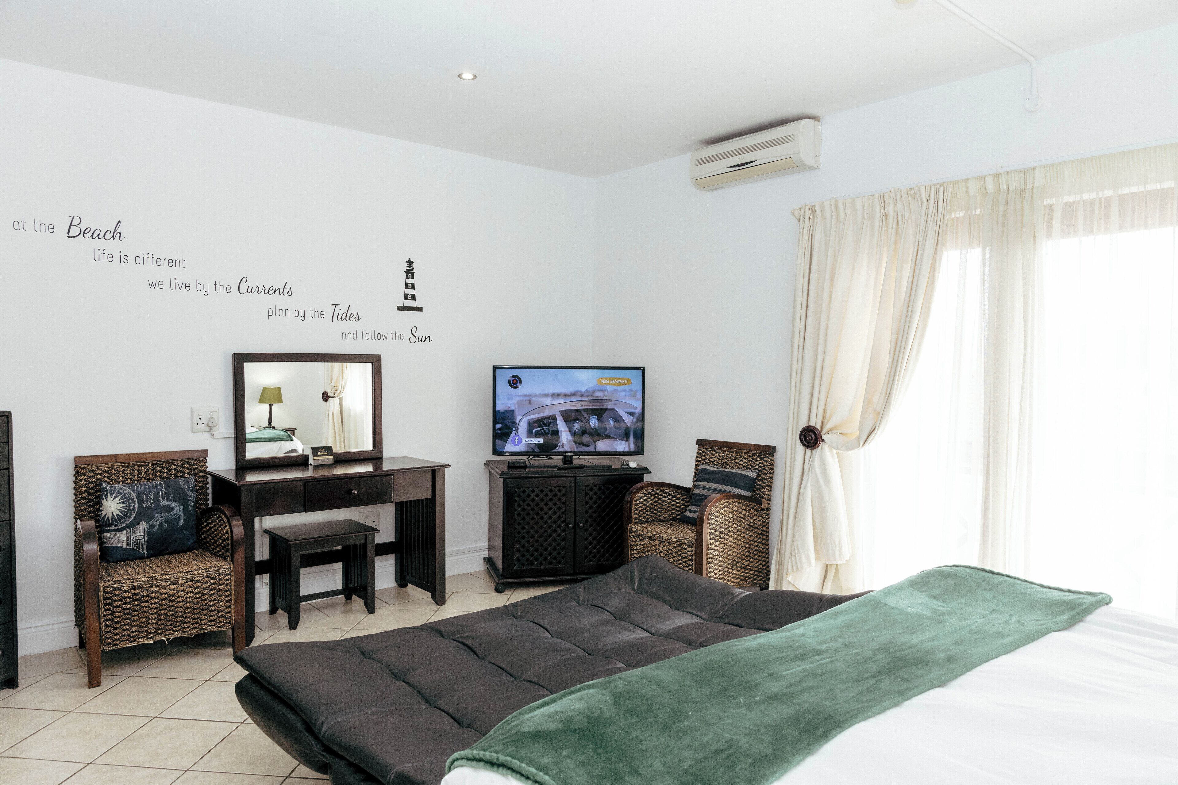 A hotel room with a bed, a desk, a chair, a television, and a wall with decorative text and a lighthouse illustration.