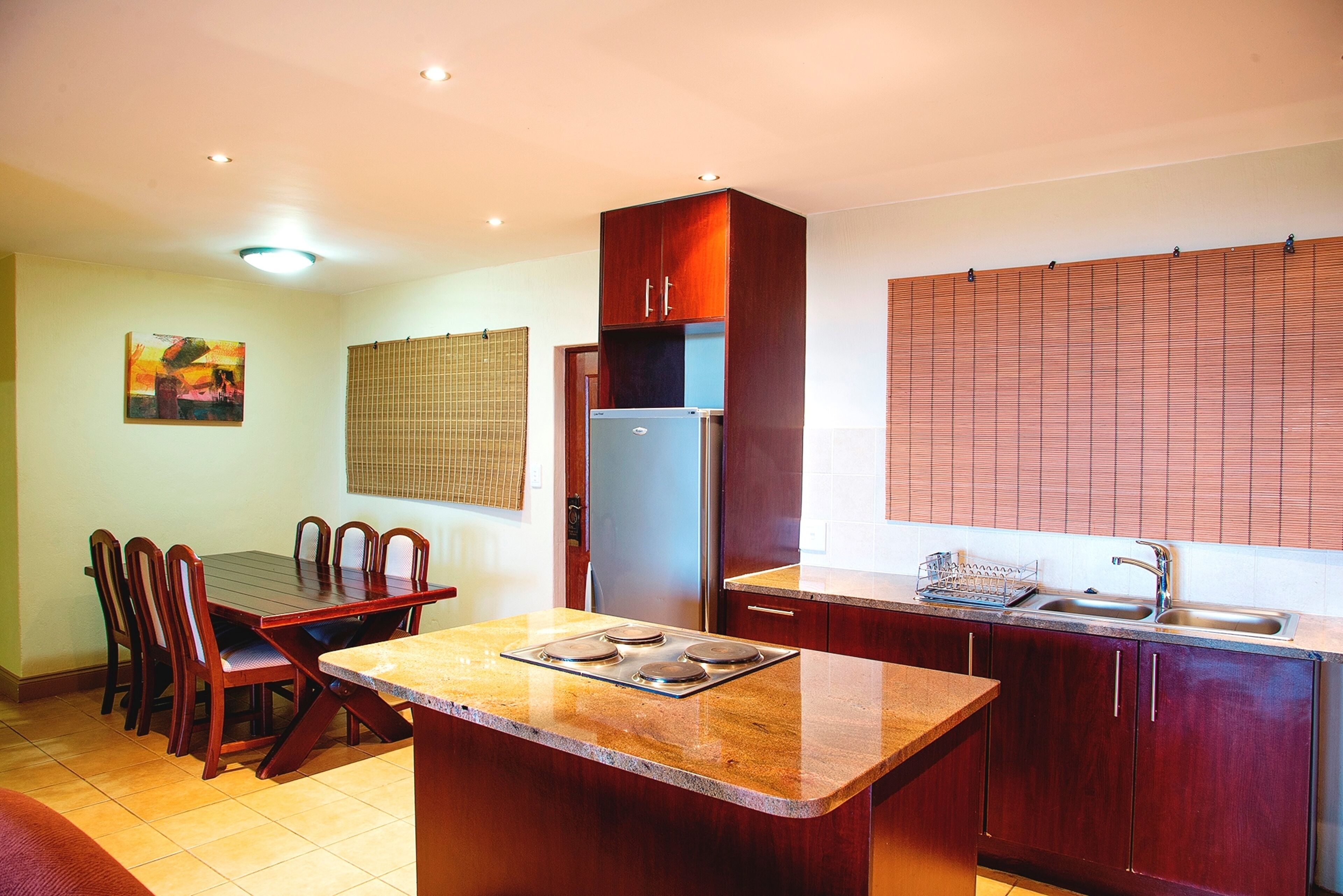 A compact kitchen with a dining table, chairs, a refrigerator, and a sink.