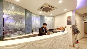 A reception desk with a modern design, a no smoking sign, and a potted plant. - Good Times (New Delhi)