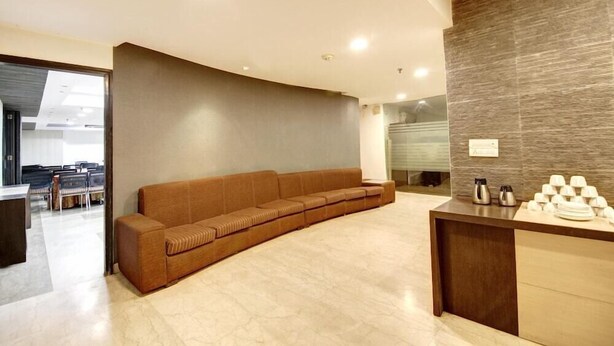 A modern reception area with a curved sofa, a reception desk, and a wall-mounted coffee station. - Good Times (New Delhi)