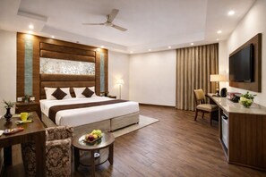 Habitación de hotel con cama, escritorio, silla, televisor y ventilador de techo.