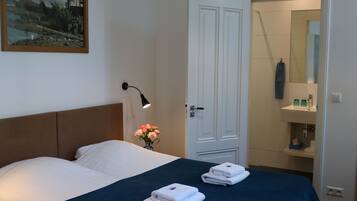 A hotel room with a bed, a nightstand with a lamp, a vase of flowers, and a bathroom visible through an open door.