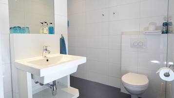 Un baño moderno con un lavamanos blanco, inodoro y zona de ducha.
