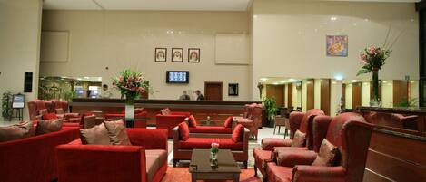 A lobby with red sofas, a reception desk, and a TV screen.