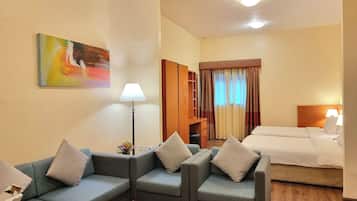 Une chambre d’hôtel avec un canapé, une petite table avec des magazines, une lampe, un lit et un tableau au mur.