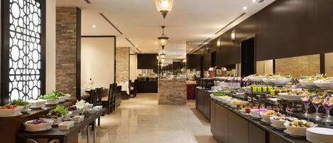 A buffet with various food items and a seating area with tables and chairs.