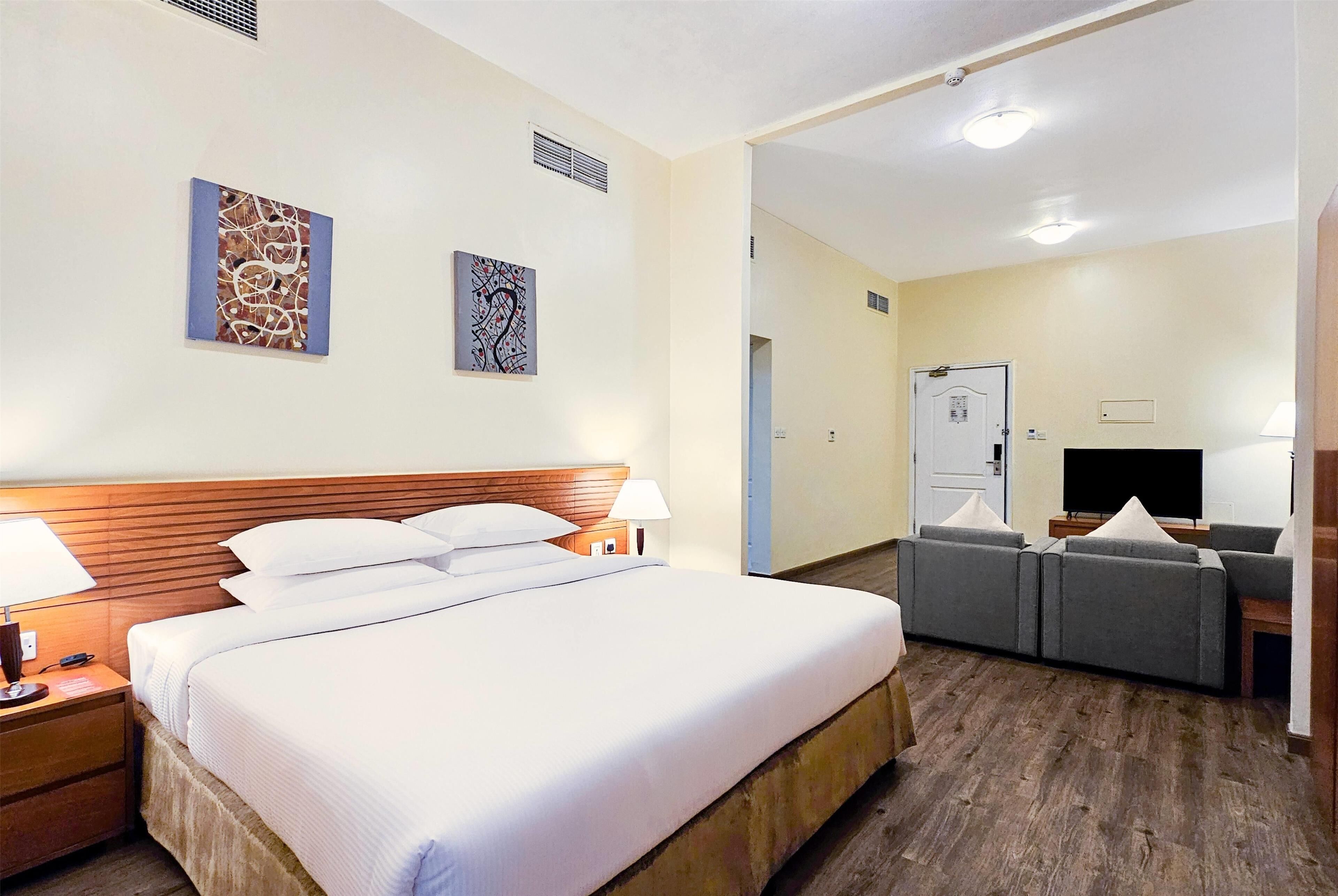 A hotel room with a large bed, a wooden headboard, a TV, and a seating area with sofas.