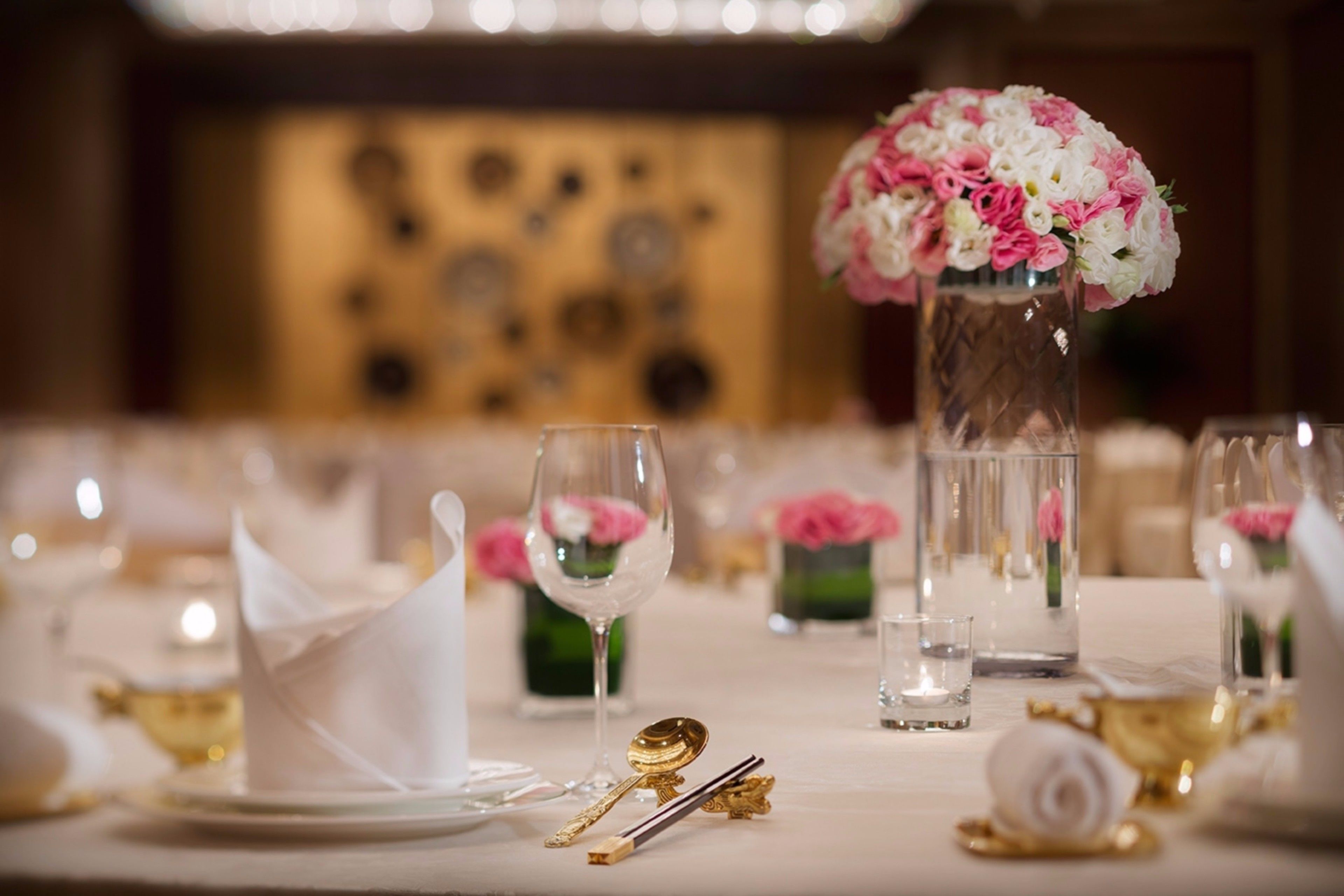 A table set with white plates, gold cutlery, and a vase of pink and white flowers.