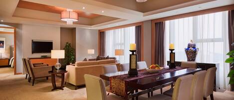 A hotel room with a dining area, a sofa, a TV, and a large window with curtains.