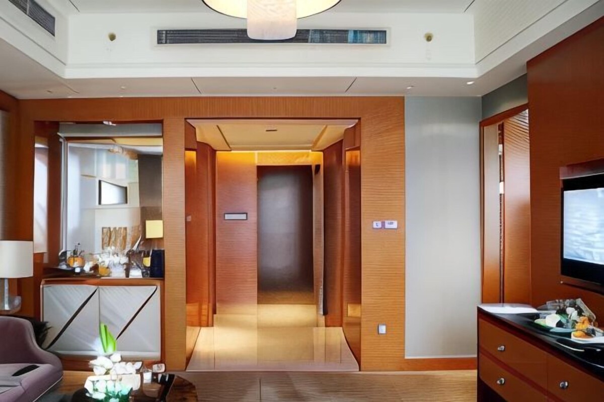 A hotel lobby with a reception desk, a television, and a hallway leading to rooms.