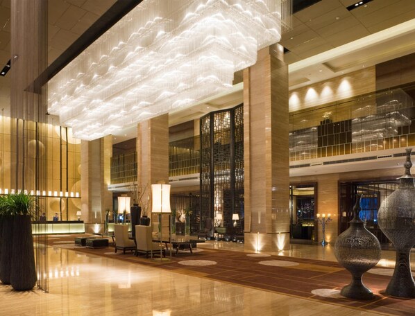 Un hall d’entrée spacieux avec un plafond haut, un comptoir de réception, un espace salon et de grands vases décoratifs.