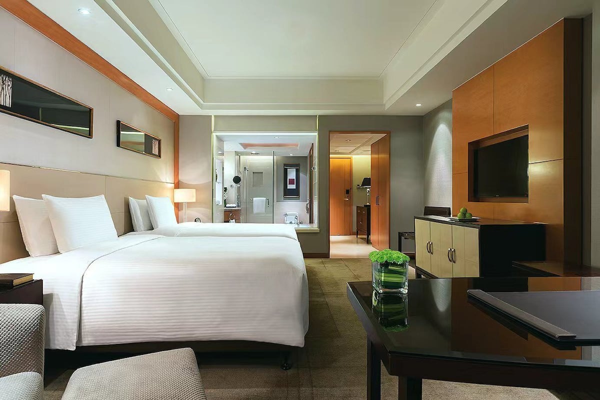A hotel room with two beds, a TV, a desk, and a bathroom visible through an open door.