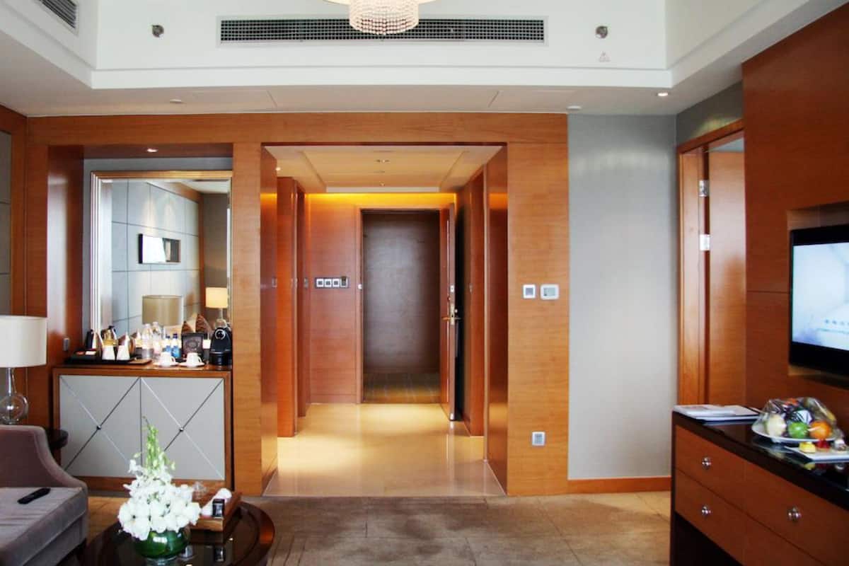 A hotel lobby with a reception desk, a seating area with a sofa and a coffee table, a TV on the right, and a hallway leading to the rooms.