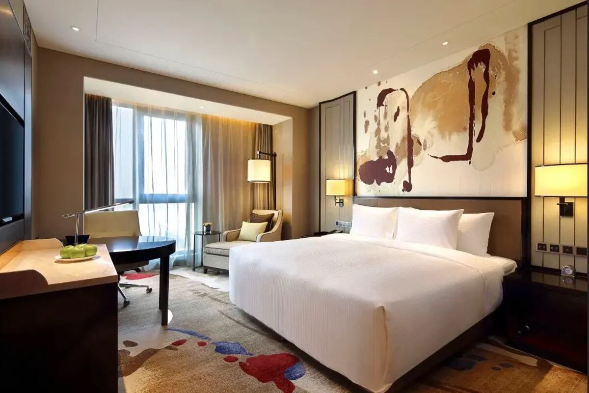 A hotel room with a large bed, a desk, a chair, a TV, and a painting on the wall.