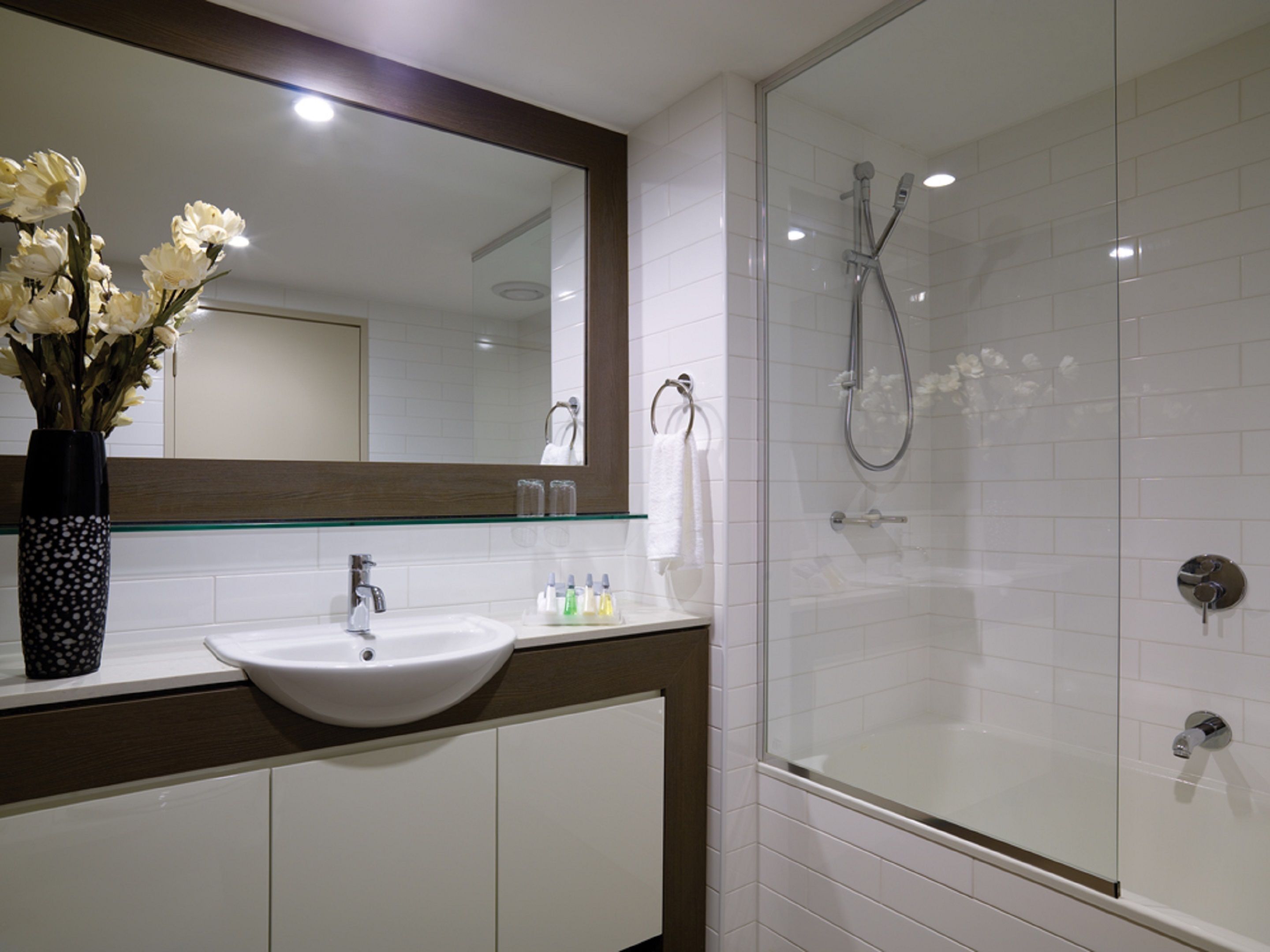 A modern bathroom with a white sink, a large mirror, and a glass-enclosed shower.