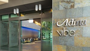 Una entrada de hotel moderna con puertas de vidrio, un área de descanso con sillas y mesas, y un letrero que dice 