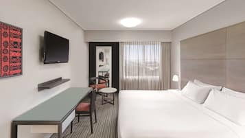 A hotel room with a bed, a desk, a chair, a TV, and a window with curtains.
