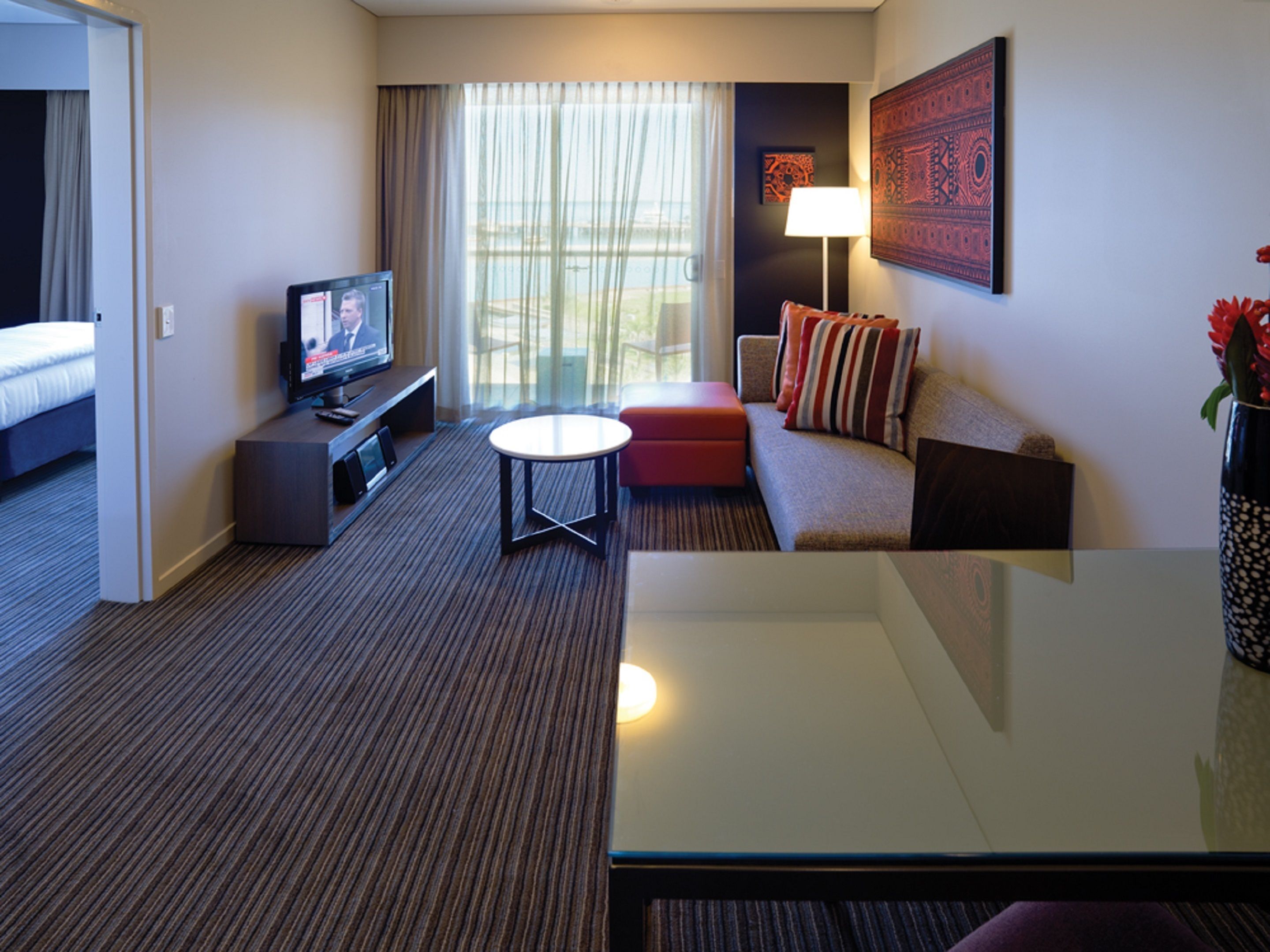 A hotel room with a bed, a TV, a sofa, a small table, and a window with curtains.