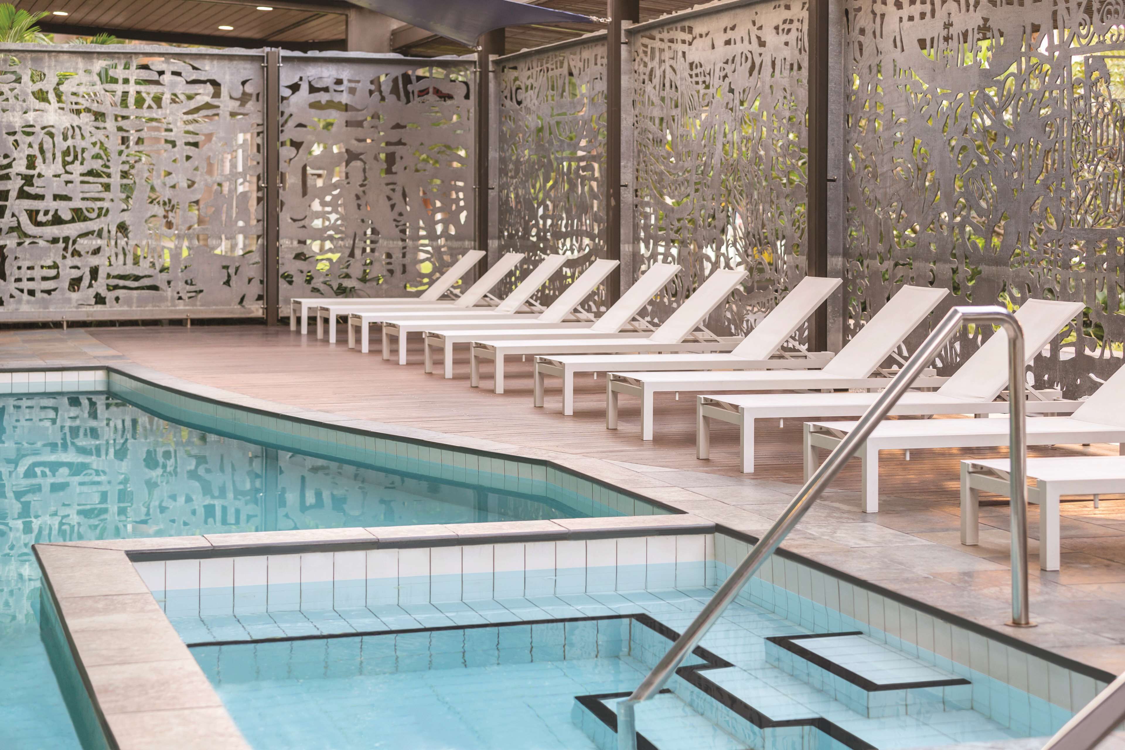 A swimming pool with white lounge chairs and a decorative wall.