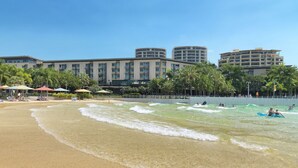 Una playa con aguas cristalinas, sombrillas y un hotel al fondo.