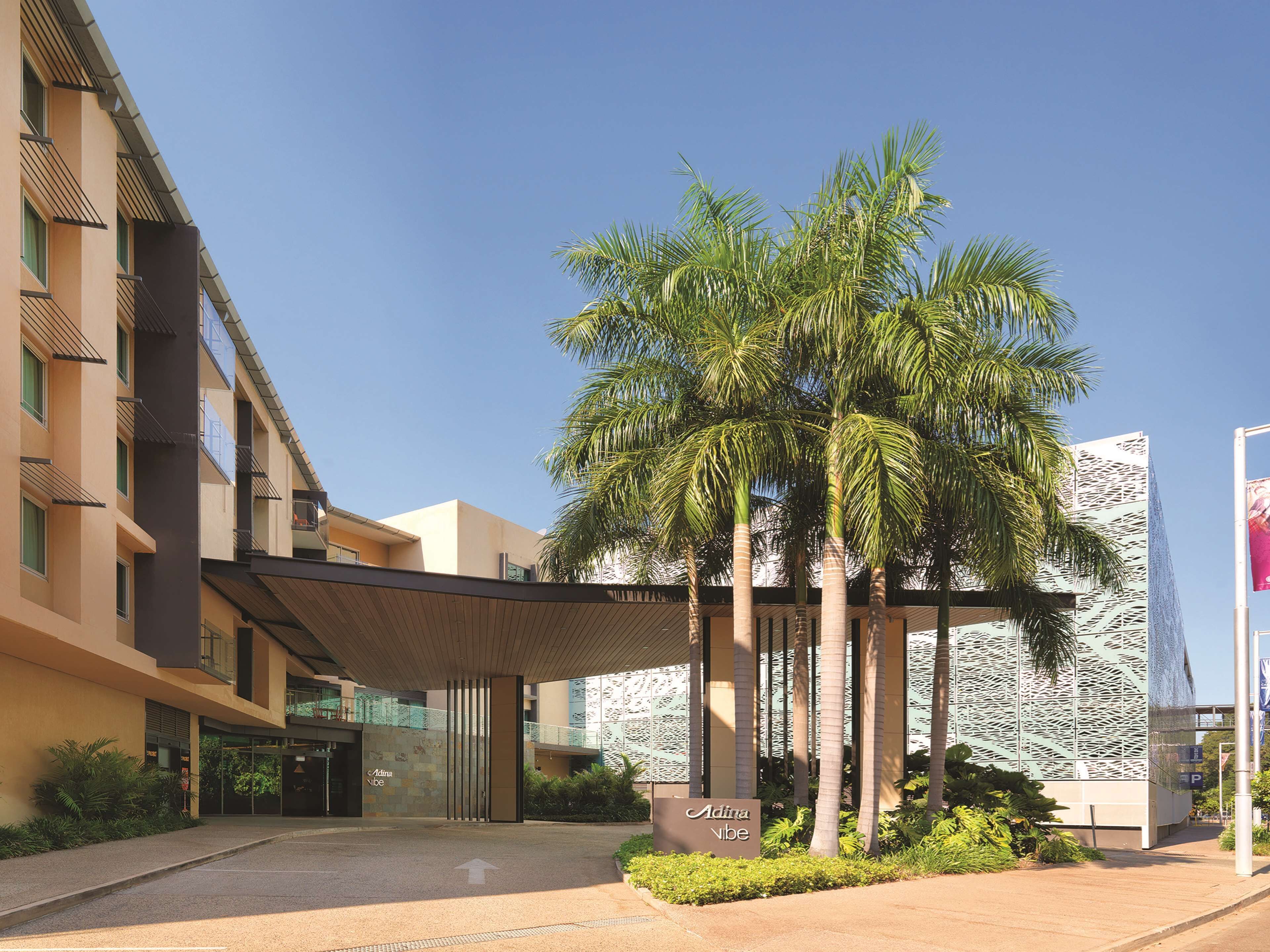 Un edificio moderno con vestíbulo cubierto, palmeras y un letrero que dice 