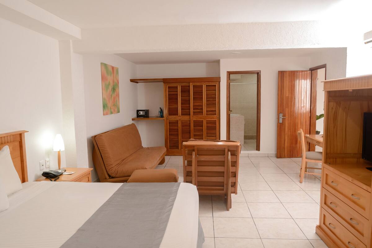 A hotel room with a bed, a sofa, a wooden desk, a television, and a wardrobe.