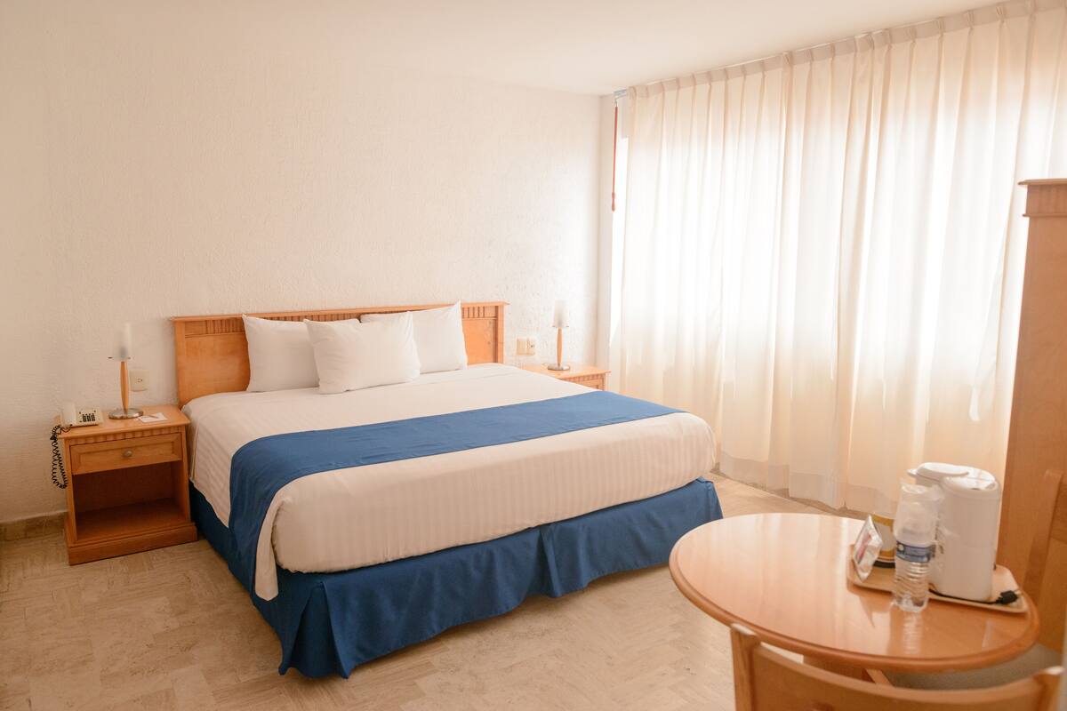 A hotel room with a bed, bedside tables, a desk, and a chair.