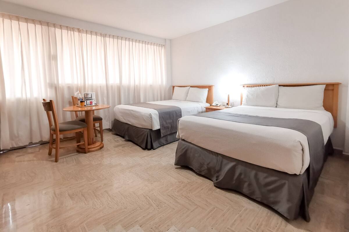 A hotel room with two beds, a small table, and a chair.
