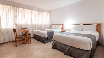 A hotel room with two beds, a small table, and a chair.
