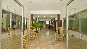 Un pasillo de hotel con sillas de madera, piso pulido y puertas de vidrio a ambos lados.