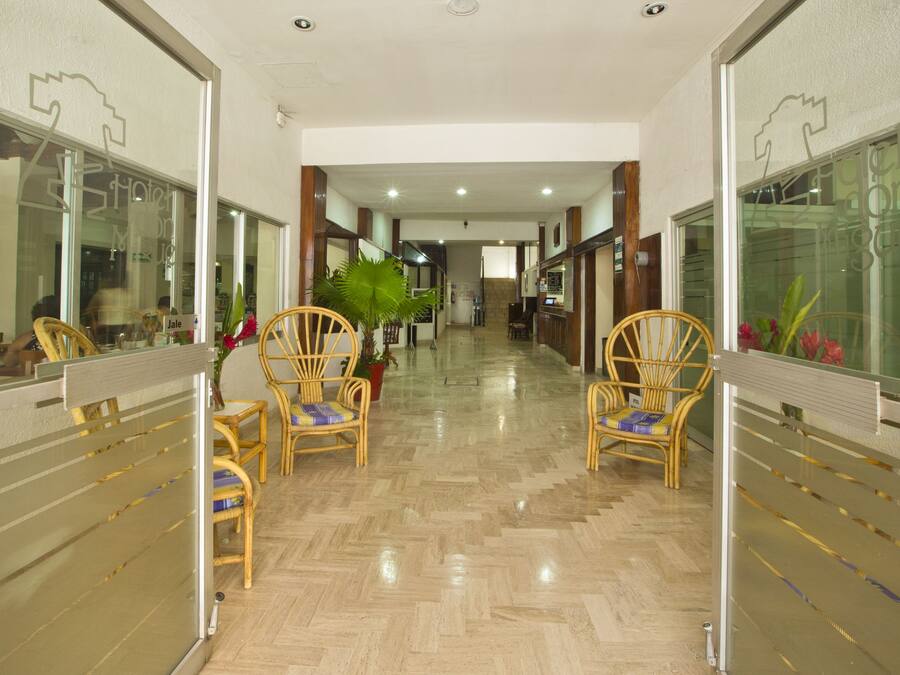 Corredor de hotel com cadeiras de madeira, piso lustroso e portas de vidro de ambos os lados.
