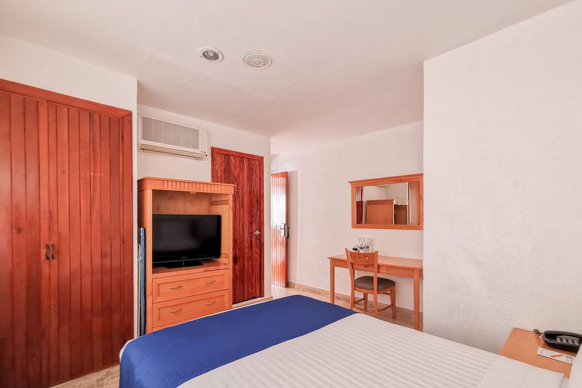 A hotel room with a bed, a desk with a chair, a television, and a wardrobe.