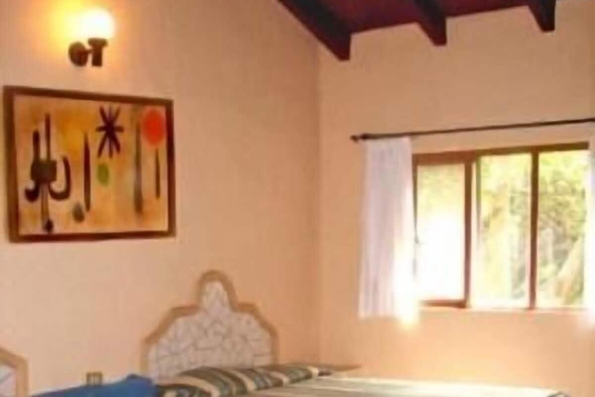 A room with two beds, a painting on the wall, and a window with curtains.