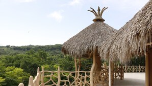 Una estructura de techo de paja con un diseño único, rodeada por una cerca blanca y ubicada en un paisaje verde exuberante.