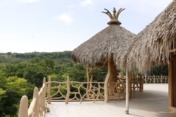 A thatched-roof structure with a unique design, surrounded by a white fence and set against a lush green landscape. - Hotel Carrizal Spa (Apazapan)