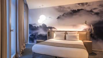 Habitación de hotel con una cama grande, una mesita de noche, una lámpara y un mural en la pared con nubes.