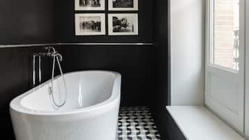 A modern bathroom with a freestanding bathtub, black and white patterned floor tiles, and framed photographs on the wall.
