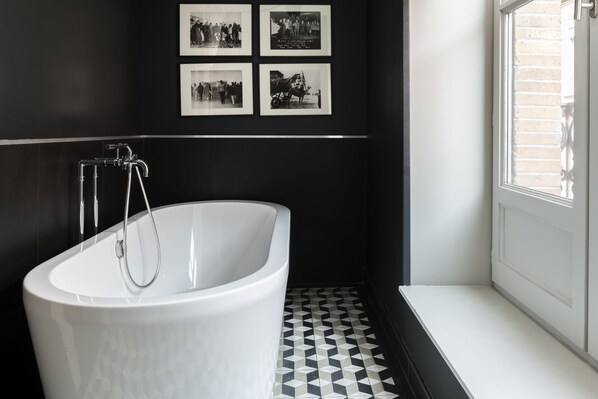 Une salle de bain moderne avec une baignoire sur pieds, des carreaux de sol noirs et blancs formant un motif, et des photographies encadrées accrochées au mur.