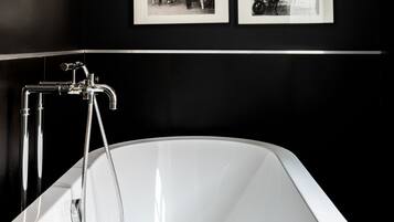 Une salle de bain moderne avec une grande baignoire blanche, des murs recouverts de carreaux noirs et un motif géométrique sur le sol.