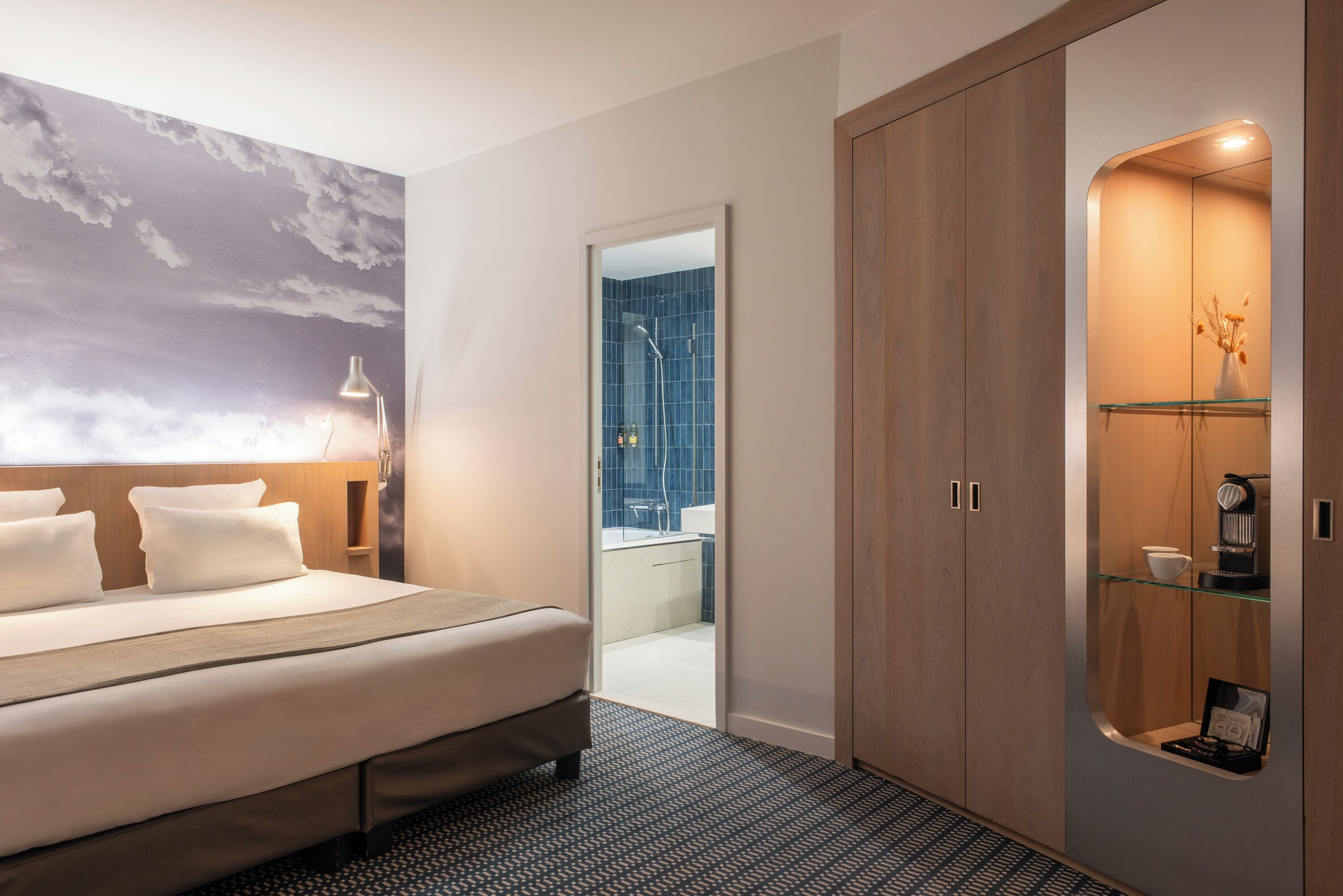 Una habitación de hotel moderna con una cama grande, una mesita de noche, un espejo y un armario.