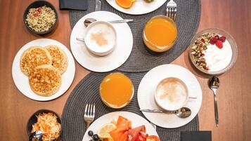 Una escena de desayuno con diversos platos, entre ellos cruasanes, panqueques, huevos revueltos y frutas frescas.