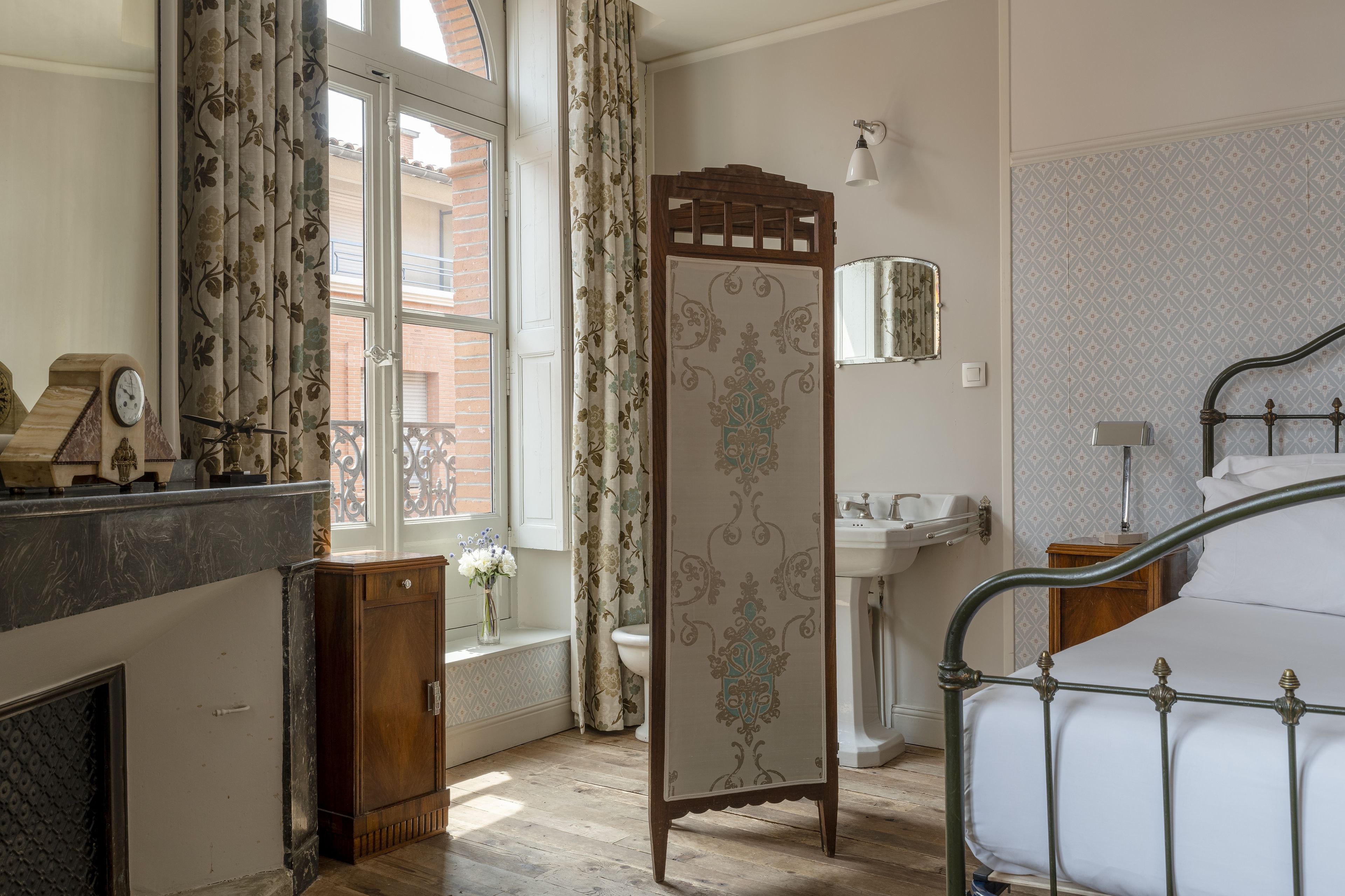 A bedroom with a bed, a wooden cabinet, a mirror, a window with curtains, and a bathroom with a sink.