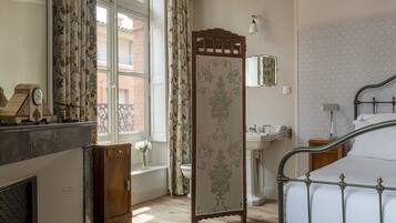 A bedroom with a bed, a wooden cabinet, a mirror, a window with curtains, and a bathroom with a sink.