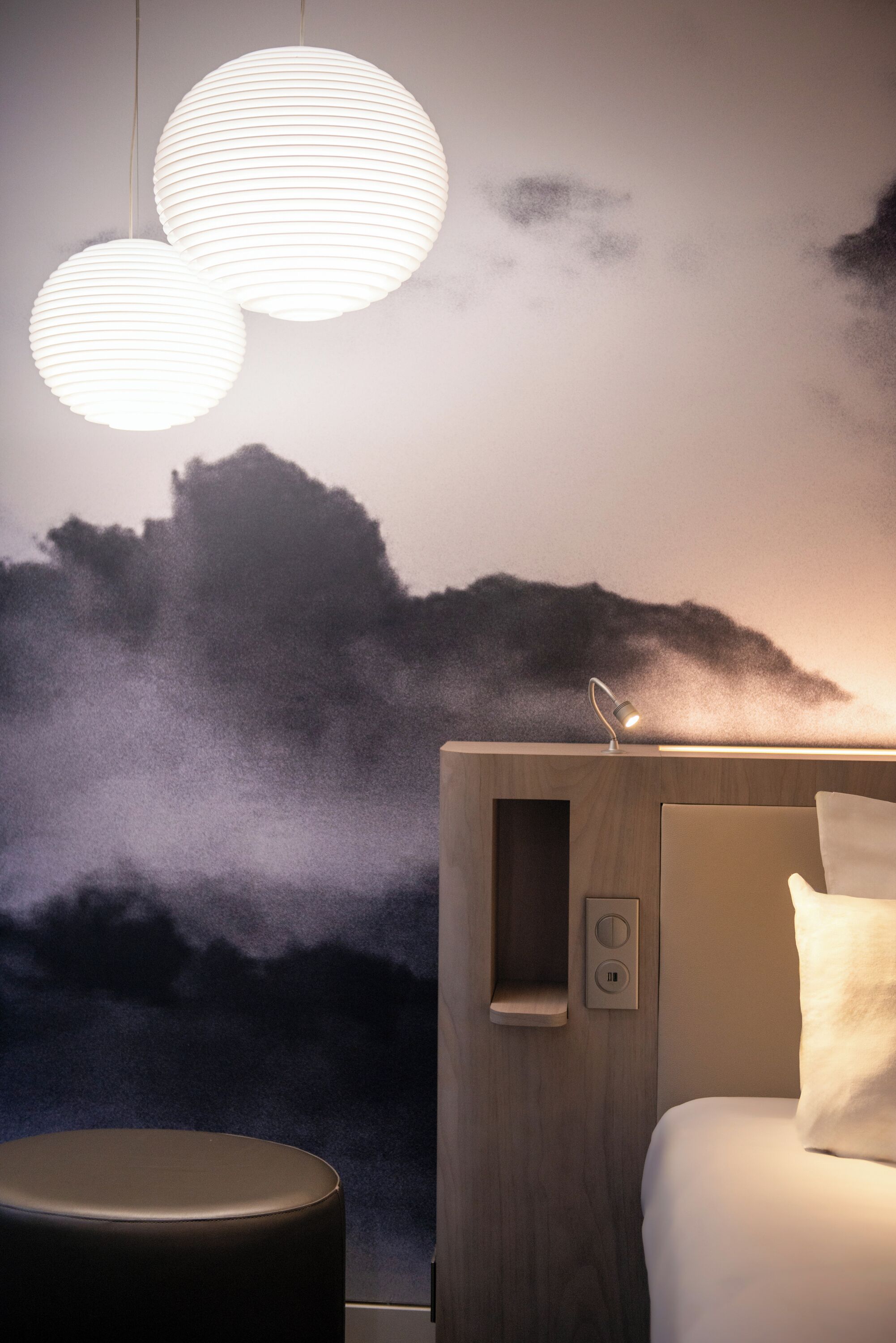 Una habitación de hotel moderna con una cama grande, una mesita de noche y un mural en la pared con un paisaje montañoso.