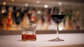 Deux verres de vin rouge sur le comptoir d’un bar, avec un arrière-plan flou composé de bouteilles.