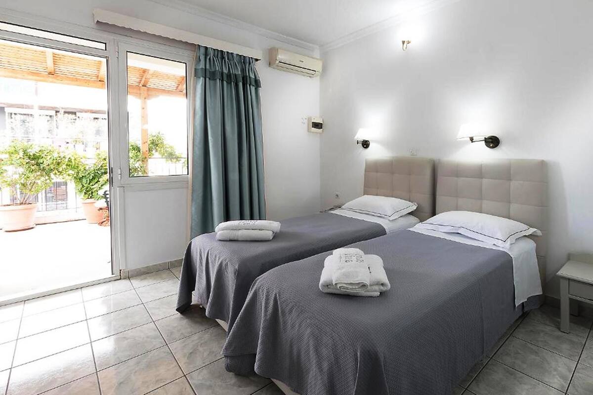 A hotel room with two beds, a sliding glass door to a balcony, and a tiled floor.
