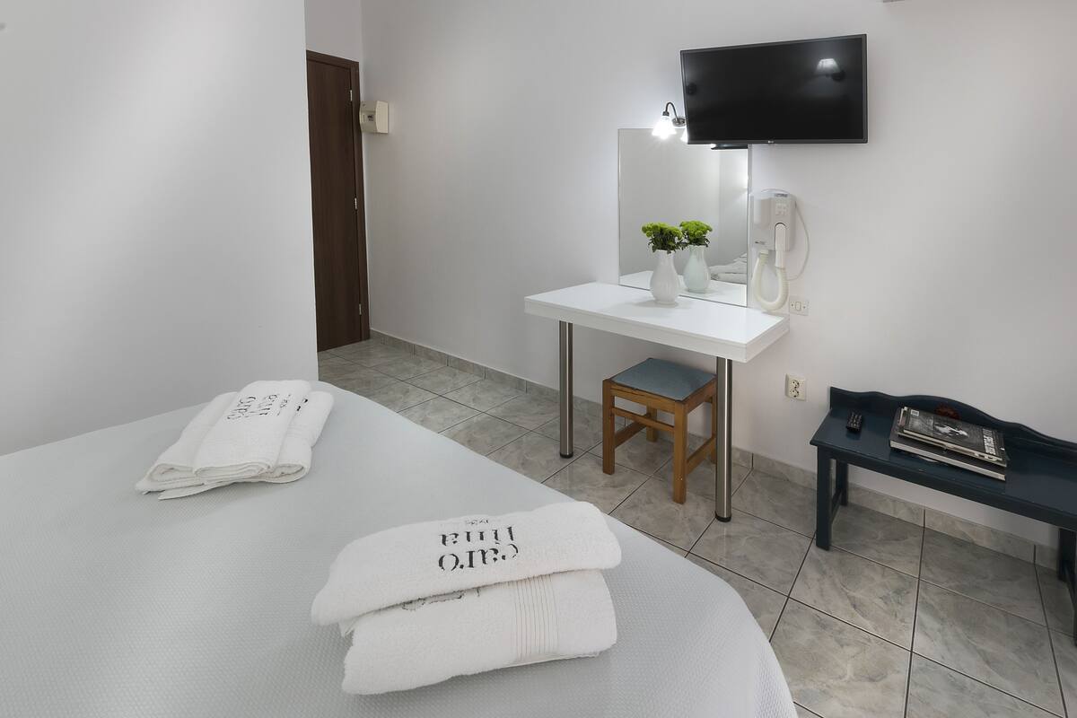 A hotel room with a bed, a desk with a chair, a TV mounted on the wall, and a small table with a remote and magazine.